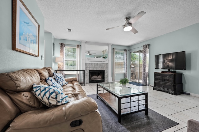 living room with a textured ceiling, a fireplace, ceiling fan, and light tile floors