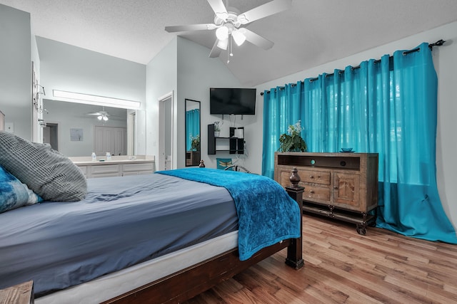 bedroom with vaulted ceiling, light hardwood / wood-style flooring, ensuite bathroom, ceiling fan, and a textured ceiling