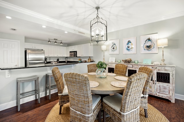 dining room with a notable chandelier, dark wood-type flooring, rail lighting, and crown molding