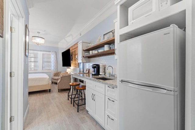 kitchen featuring white fridge, backsplash, ornamental molding, light wood-type flooring, and sink