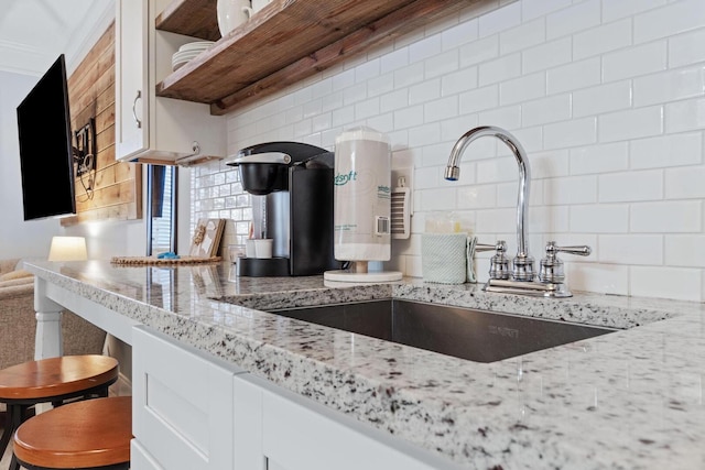 kitchen with crown molding, light stone counters, backsplash, sink, and white cabinetry