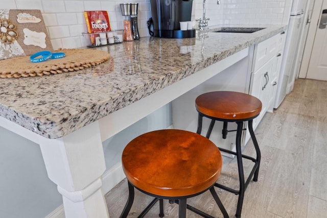 kitchen with light stone countertops, light wood-type flooring, backsplash, sink, and white cabinets