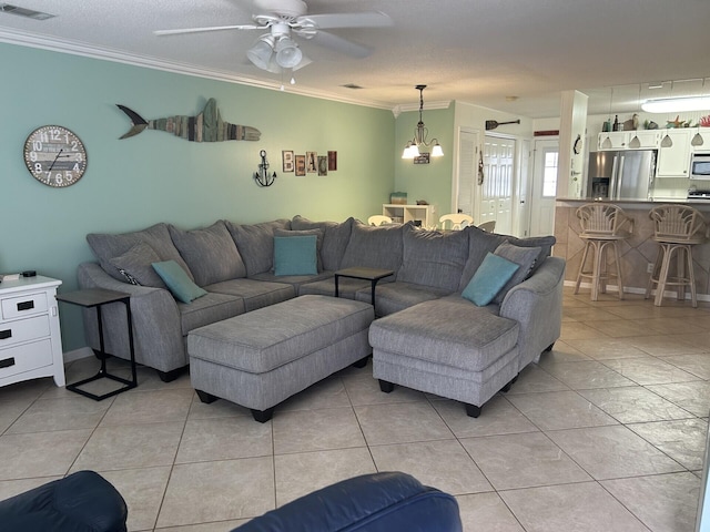 living room featuring ceiling fan with notable chandelier, a textured ceiling, ornamental molding, and light tile patterned flooring