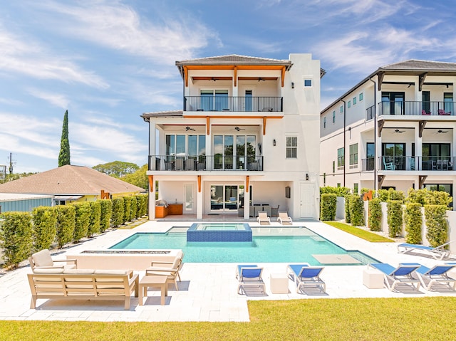 rear view of house with ceiling fan, a pool with hot tub, an outdoor hangout area, a balcony, and a patio