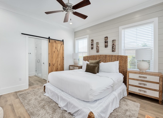 bedroom featuring wood walls, ceiling fan, a barn door, and light hardwood / wood-style flooring