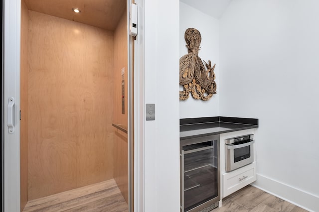 kitchen with light wood-type flooring, beverage cooler, white cabinetry, elevator, and oven