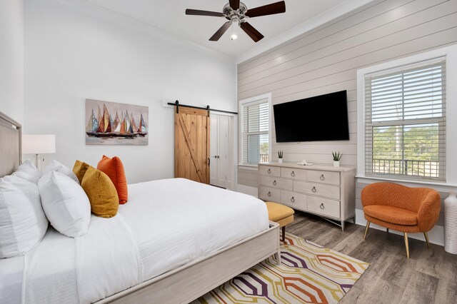 bedroom featuring dark hardwood / wood-style flooring, ornamental molding, ceiling fan, wooden walls, and a barn door