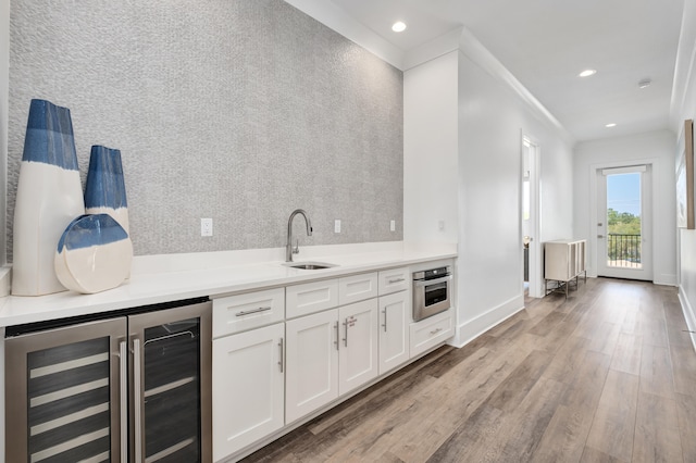 kitchen with wine cooler, ornamental molding, stainless steel oven, sink, and white cabinetry