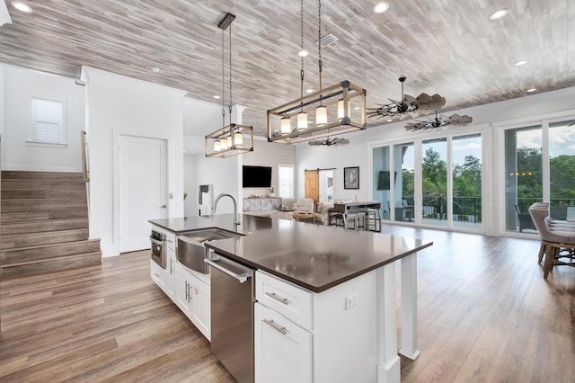 kitchen featuring stainless steel dishwasher, sink, a barn door, a center island with sink, and white cabinets