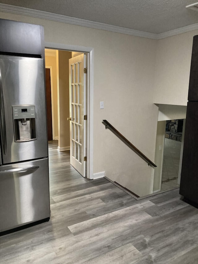 kitchen with a textured ceiling, ornamental molding, stainless steel fridge, and wood-type flooring