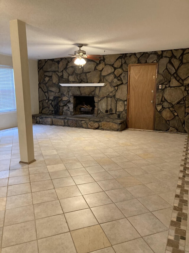 unfurnished living room with a stone fireplace, a textured ceiling, ceiling fan, and light tile floors