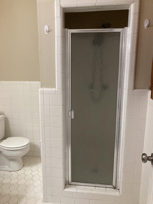 bathroom featuring tile walls, toilet, and a shower with door