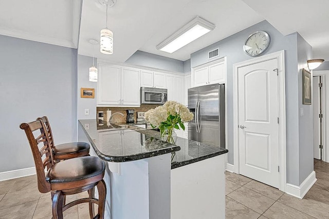 kitchen featuring appliances with stainless steel finishes, a breakfast bar area, white cabinets, hanging light fixtures, and kitchen peninsula