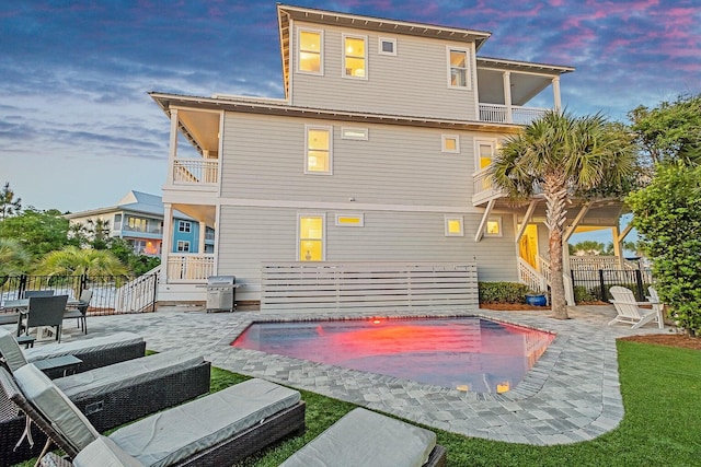 back house at dusk featuring a fenced in pool, a patio area, and a balcony