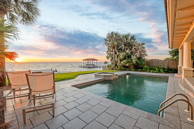 pool at dusk featuring a patio, an in ground hot tub, and a water view