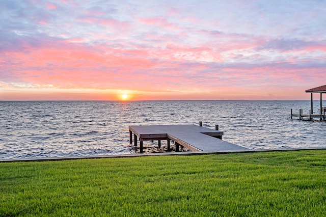 view of dock with a lawn and a water view