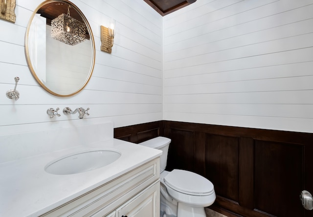 bathroom with wood walls, toilet, and vanity