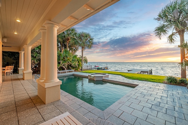 pool at dusk with a patio, an in ground hot tub, and a water view