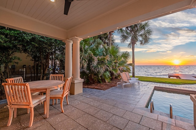 patio terrace at dusk featuring ceiling fan and a water view