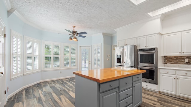 kitchen with stainless steel appliances, backsplash, ceiling fan, crown molding, and white cabinetry