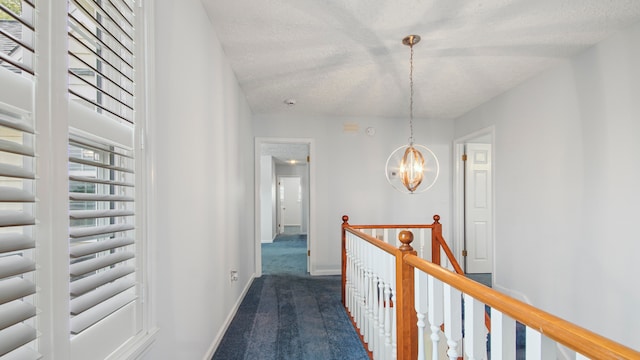 corridor featuring a notable chandelier, a textured ceiling, and dark colored carpet