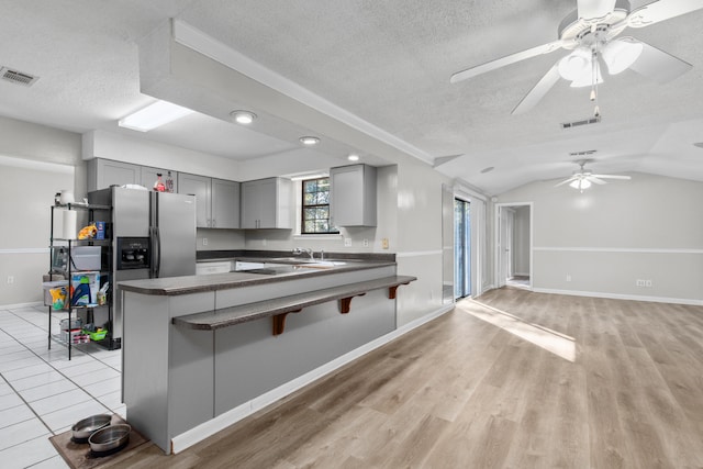 kitchen with lofted ceiling, light wood-type flooring, gray cabinets, kitchen peninsula, and ceiling fan