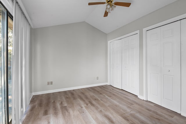 unfurnished bedroom with hardwood / wood-style floors, two closets, ceiling fan, and lofted ceiling