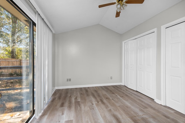 unfurnished bedroom with multiple closets, lofted ceiling, ceiling fan, and hardwood / wood-style floors