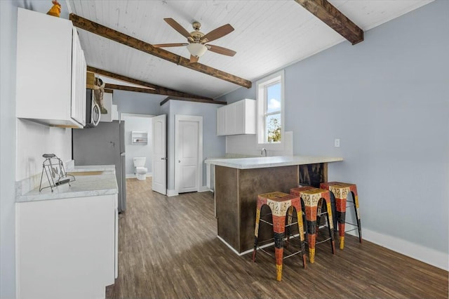 kitchen with dark wood-type flooring, white cabinets, vaulted ceiling with beams, ceiling fan, and appliances with stainless steel finishes