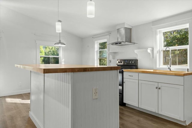 kitchen featuring wall chimney range hood, pendant lighting, electric range, white cabinetry, and plenty of natural light