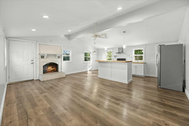 unfurnished living room featuring hardwood / wood-style floors, lofted ceiling with beams, ceiling fan, and a fireplace