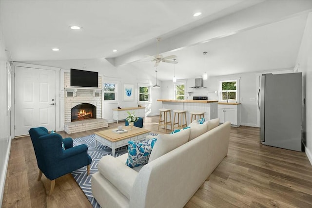 living room with lofted ceiling with beams, light hardwood / wood-style floors, ceiling fan, and a brick fireplace