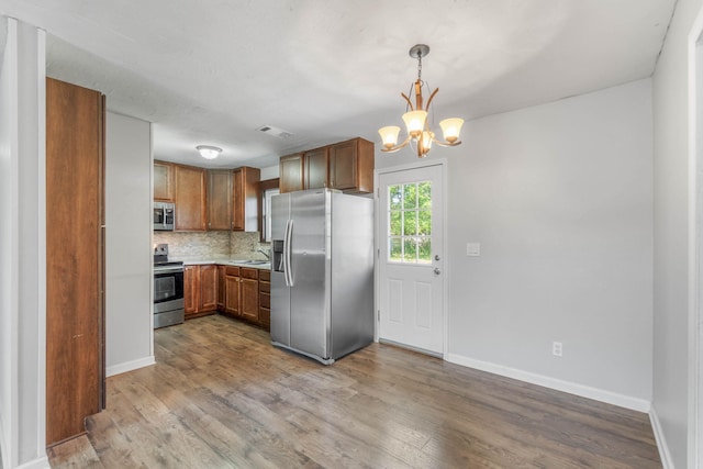 kitchen featuring sink, stainless steel appliances, tasteful backsplash, a notable chandelier, and decorative light fixtures