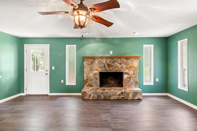 unfurnished living room with a textured ceiling, ceiling fan, a stone fireplace, and dark wood-type flooring