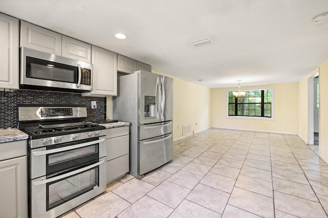 kitchen featuring appliances with stainless steel finishes, dark stone counters, light tile patterned floors, a chandelier, and gray cabinets