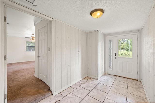 foyer with ceiling fan, wood walls, light colored carpet, a textured ceiling, and ornamental molding