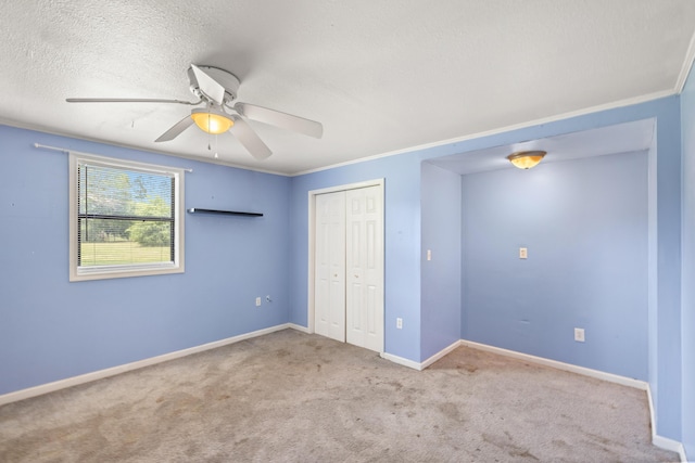 unfurnished bedroom featuring light carpet, ornamental molding, a textured ceiling, ceiling fan, and a closet