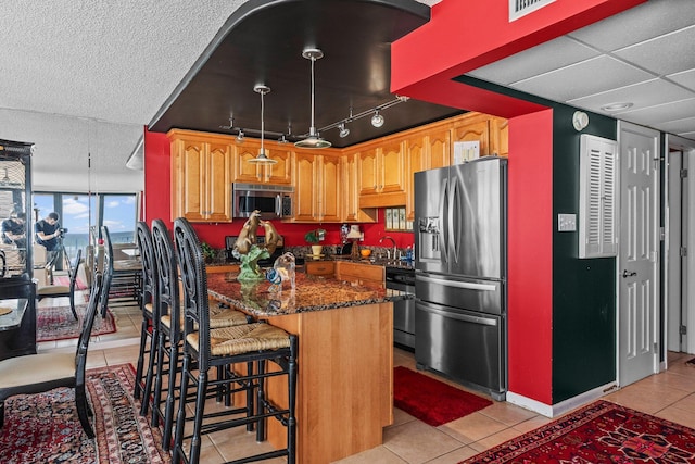 kitchen featuring dark stone countertops, track lighting, light tile floors, sink, and appliances with stainless steel finishes