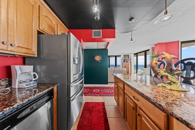 kitchen with dark stone counters, a textured ceiling, light tile flooring, and stainless steel dishwasher