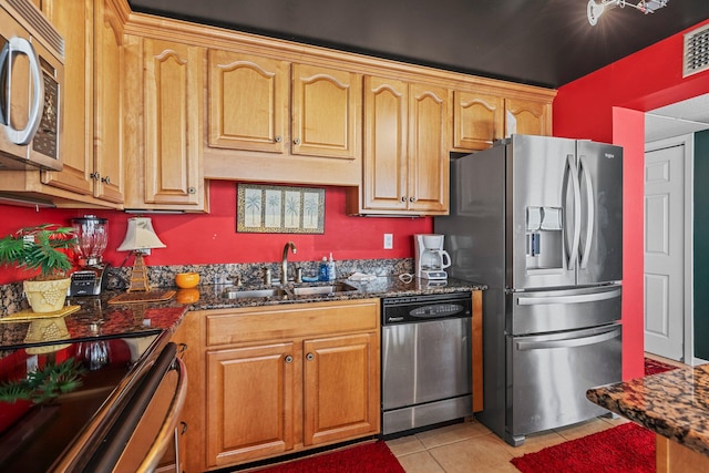 kitchen with dark stone counters, sink, light tile flooring, and stainless steel appliances