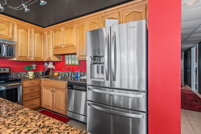 kitchen featuring tile floors, stainless steel appliances, sink, and dark stone countertops