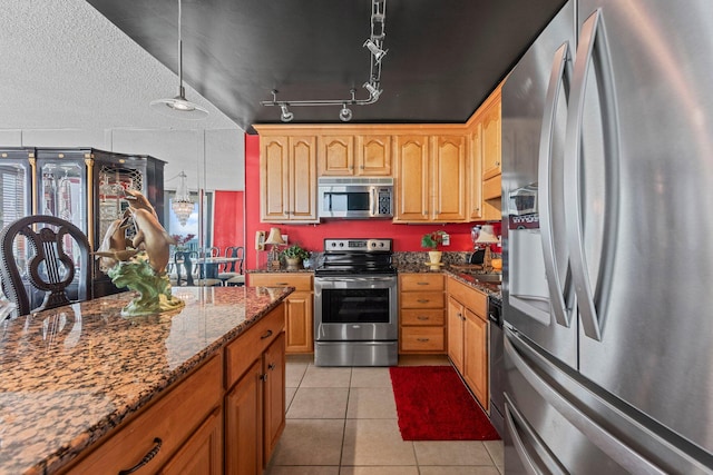 kitchen featuring stainless steel appliances, light tile flooring, dark stone countertops, rail lighting, and hanging light fixtures