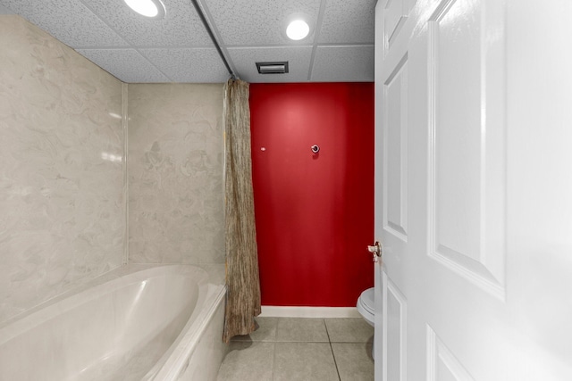 bathroom featuring tile floors, washtub / shower combination, toilet, and a drop ceiling