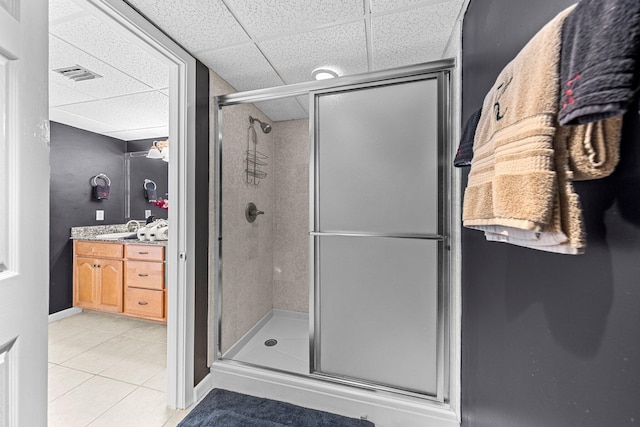 bathroom with tile flooring, a shower with shower door, vanity, and a drop ceiling