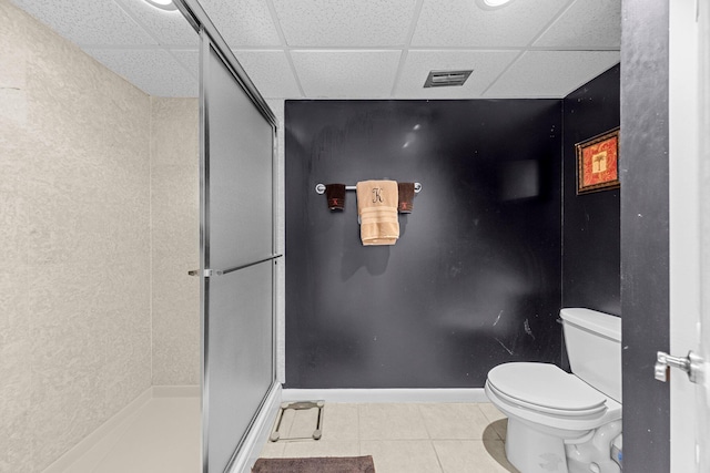 bathroom featuring tile flooring, a shower with door, toilet, and a paneled ceiling