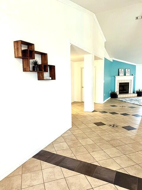 9720 Parker Lake Cir, Navarre, FL 32566 - unfurnished living room with a tiled fireplace, light tile patterned floors, crown molding, visible vents, and high vaulted ceiling