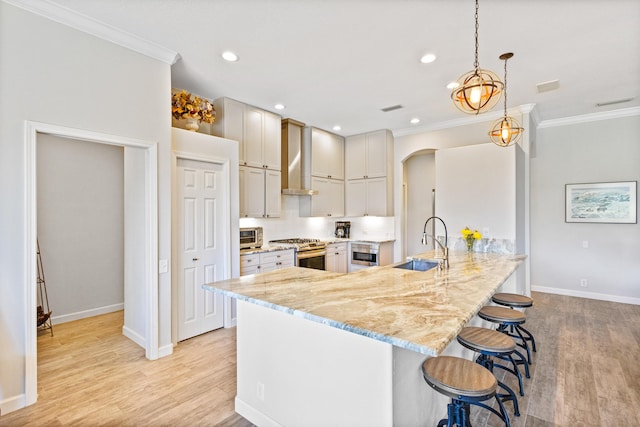 kitchen with light stone countertops, sink, wall chimney exhaust hood, stainless steel appliances, and pendant lighting