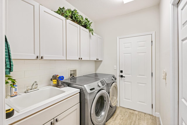 laundry area featuring washer and clothes dryer, light hardwood / wood-style flooring, cabinets, and sink