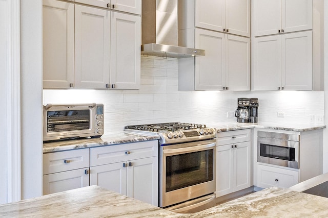 kitchen with white cabinets, wall chimney exhaust hood, tasteful backsplash, gas stove, and light stone counters