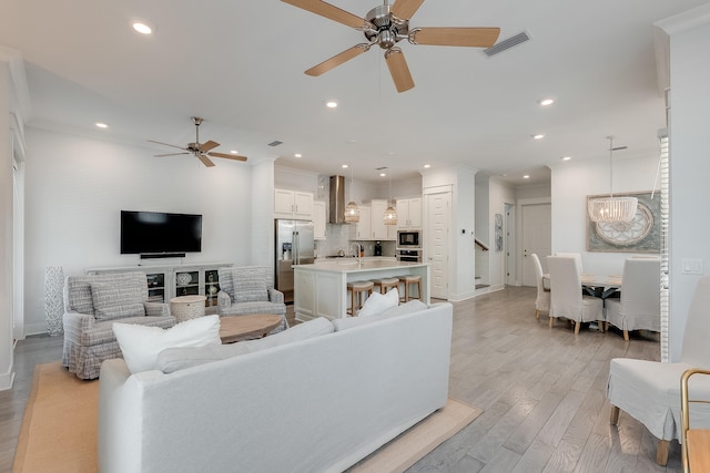 living room with ceiling fan with notable chandelier, light hardwood / wood-style floors, crown molding, and sink